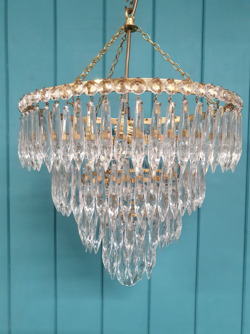 A tiered brass ceiling chandelier featuring multiple concentric rows of clear glass spike crystal prisms suspended by a chain. View V