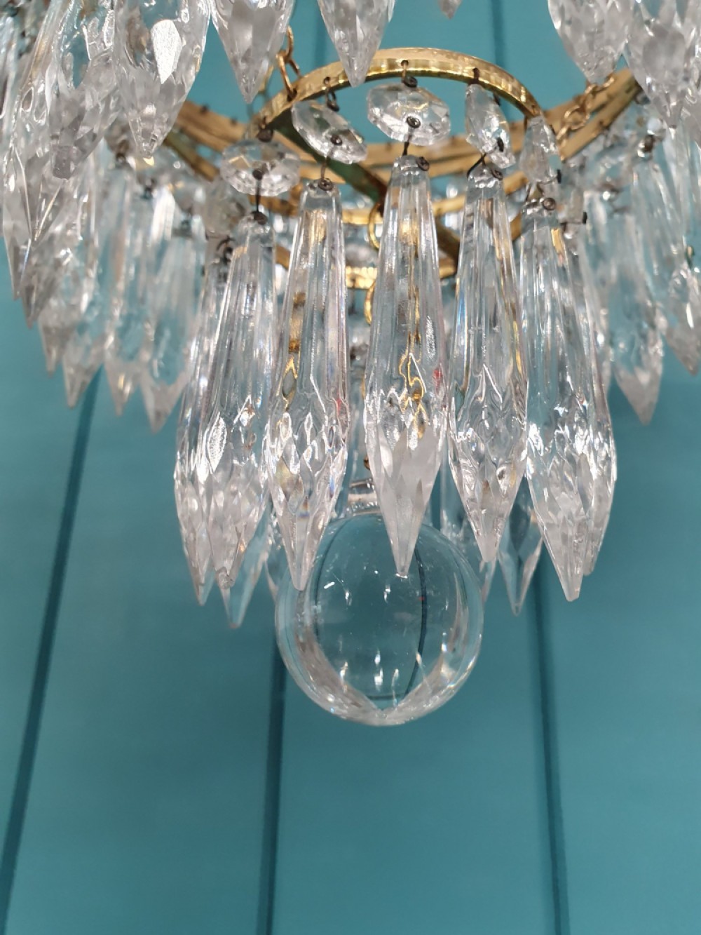 A tiered brass ceiling chandelier featuring multiple concentric rows of clear glass spike crystal prisms suspended by a chain. View VII