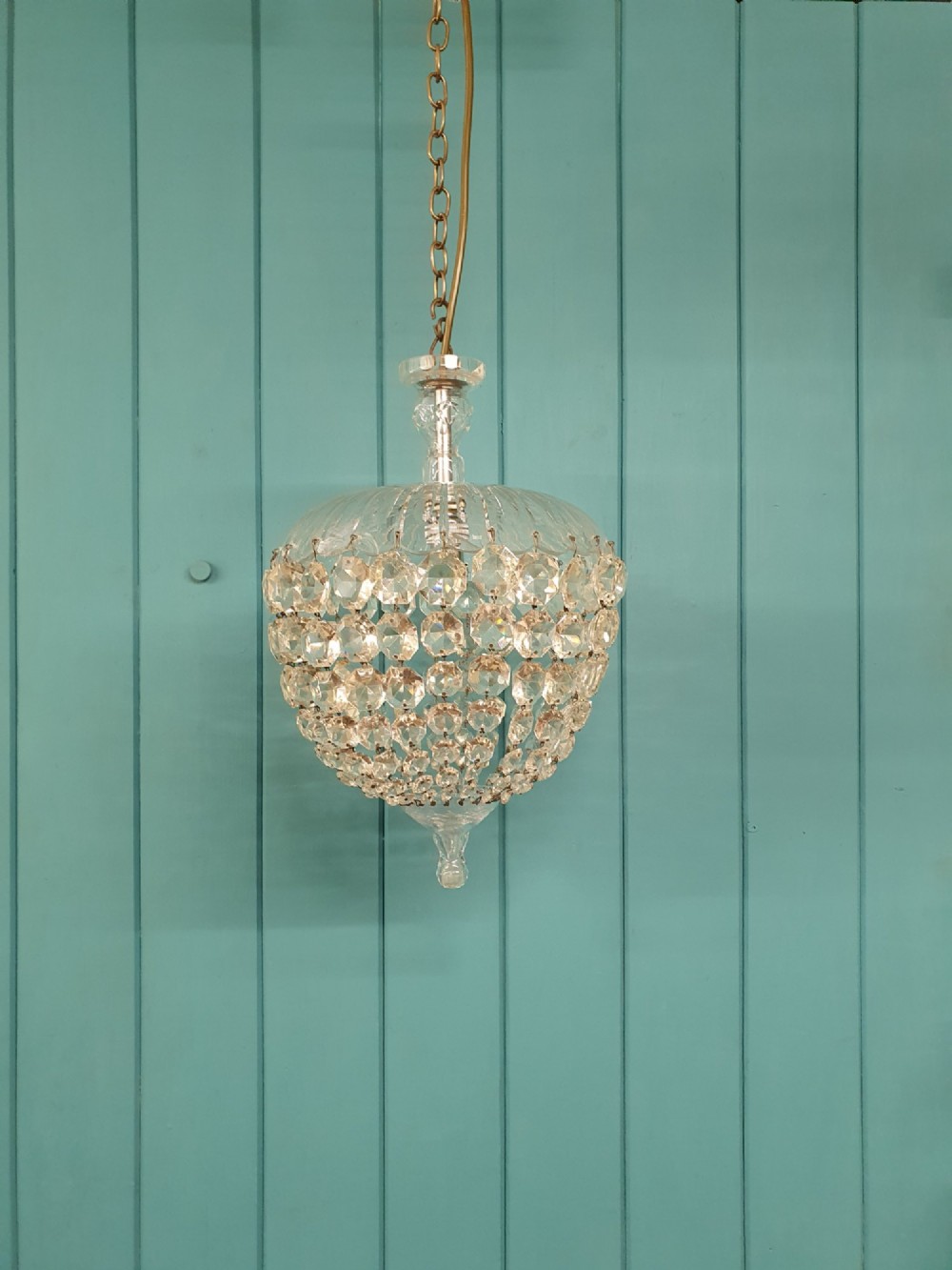 An early 20th-century dome-top chandelier with faceted crystal strands forming a rounded drop, suspended from a brass chain.