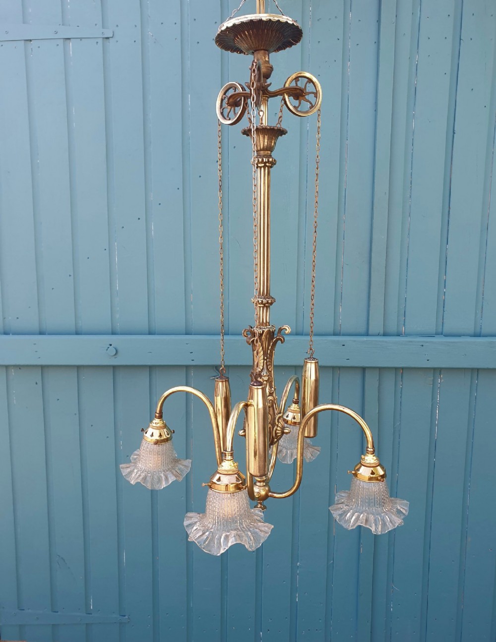 An antique brass four-arm rise and fall chandelier with curved arms, ruffled glass shades, and a counterweight pulley mechanism.