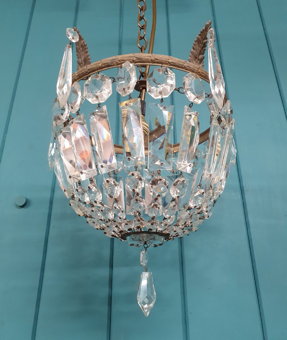 An early twentieth-century small bag-style chandelier featuring cut crystal coffin prisms, a decorative brass upper rim with leaf detail, and a suspension chain. View II