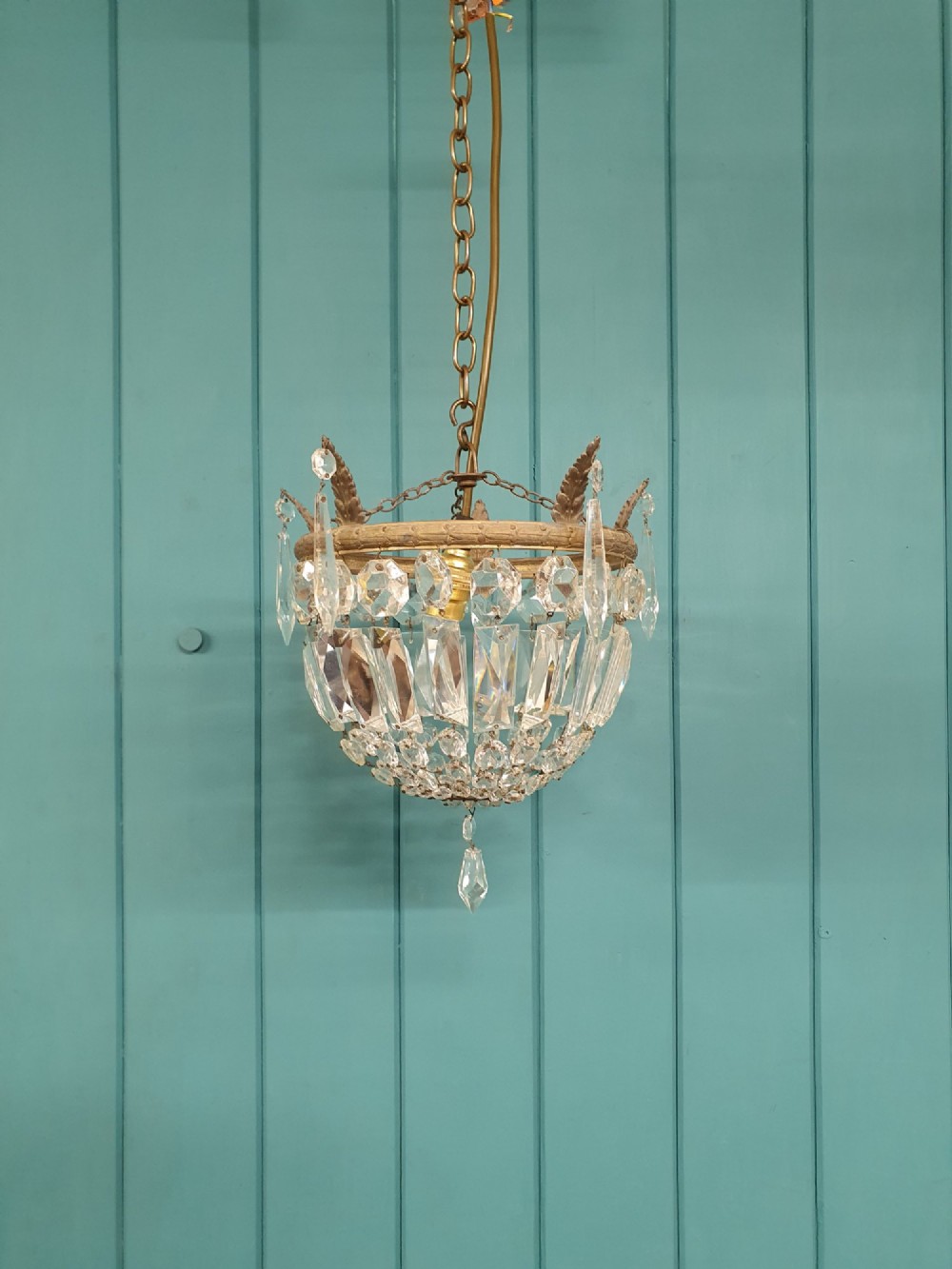 An early twentieth-century small bag-style chandelier featuring cut crystal coffin prisms, a decorative brass upper rim with leaf detail, and a suspension chain.