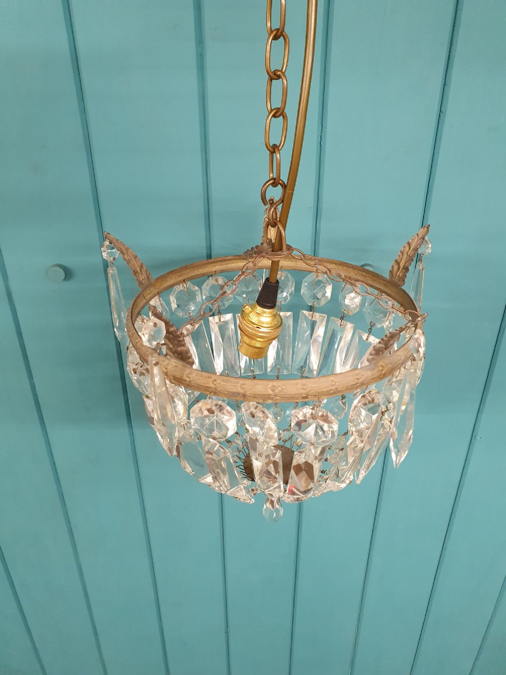 An early twentieth-century small bag-style chandelier featuring cut crystal coffin prisms, a decorative brass upper rim with leaf detail, and a suspension chain. View IV