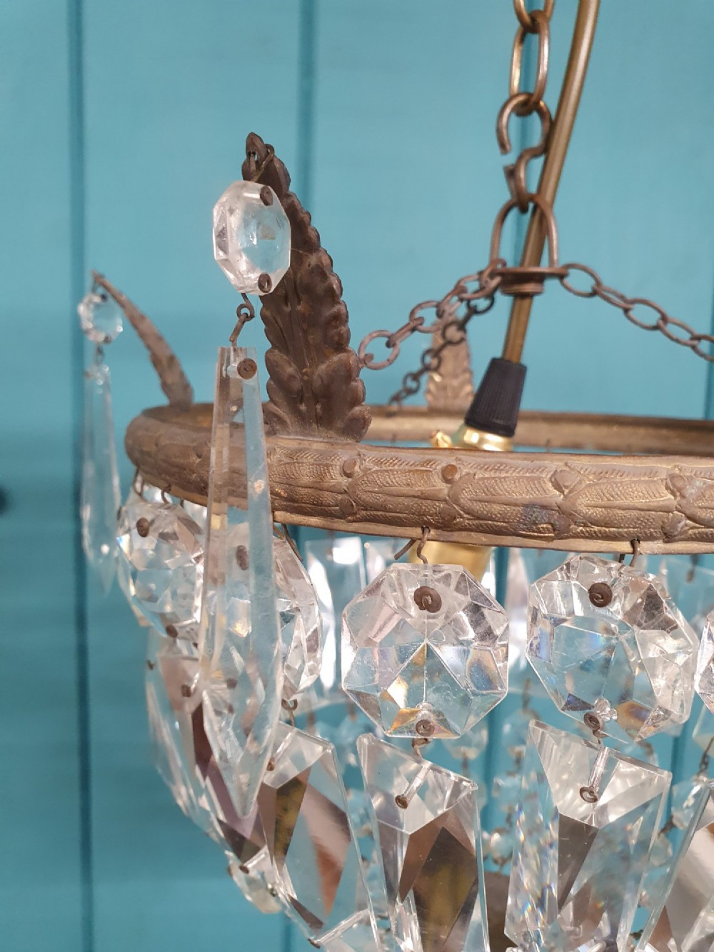 An early twentieth-century small bag-style chandelier featuring cut crystal coffin prisms, a decorative brass upper rim with leaf detail, and a suspension chain. View V