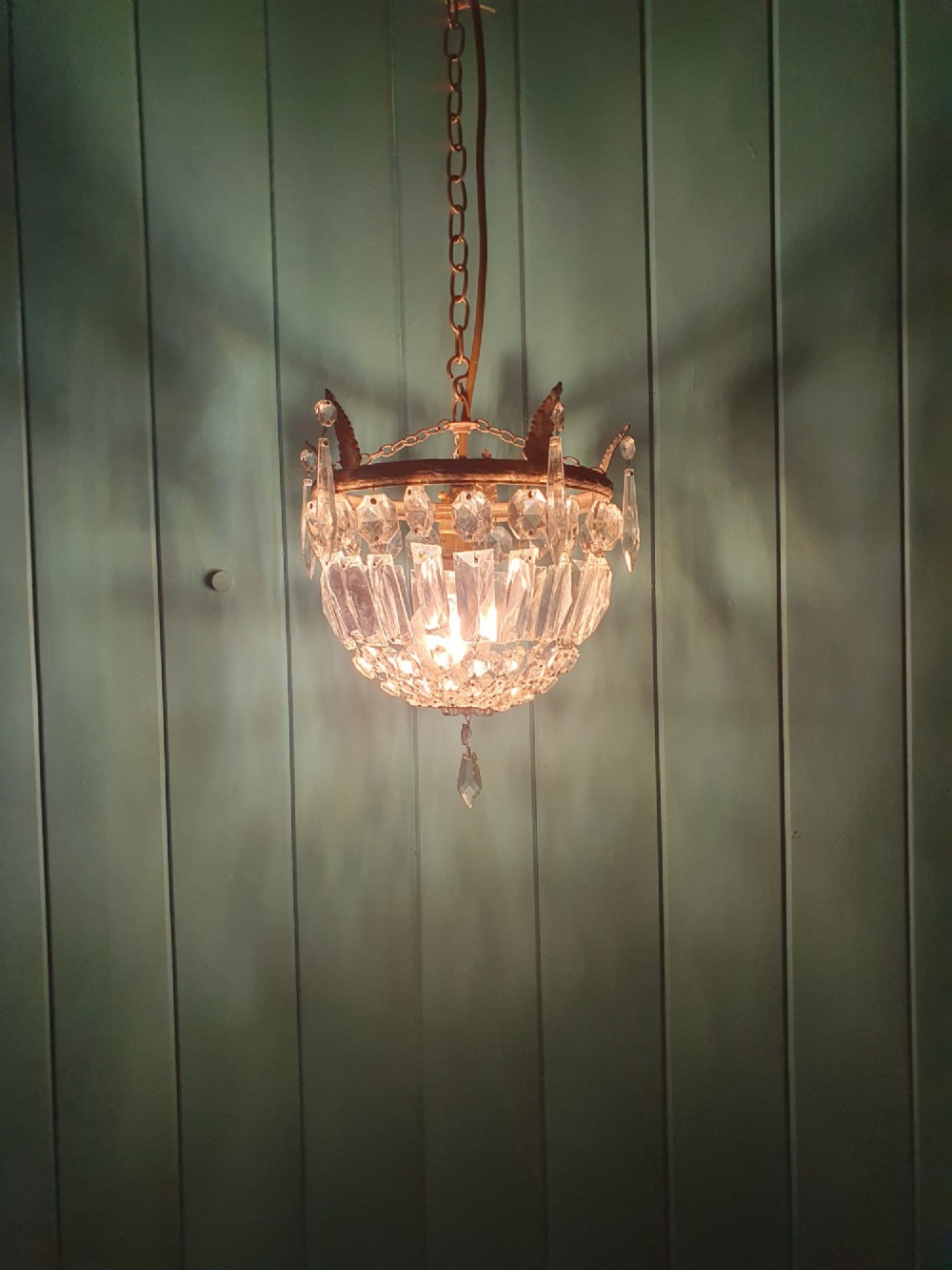 An early twentieth-century small bag-style chandelier featuring cut crystal coffin prisms, a decorative brass upper rim with leaf detail, and a suspension chain. View VI
