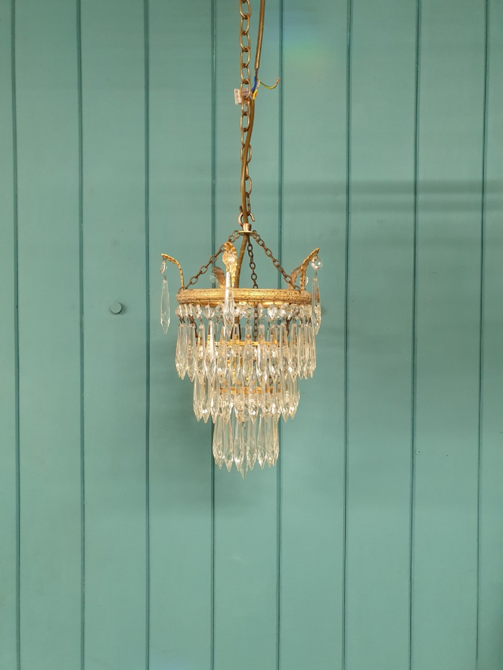 A small three-tier brass pendant chandelier with cascading clear glass icicle drops suspended from a brass chain.