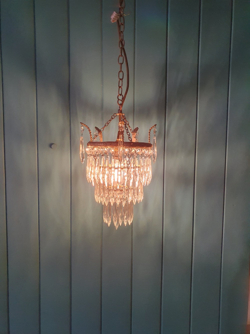 A small three-tier brass pendant chandelier with cascading clear glass icicle drops suspended from a brass chain. View VI