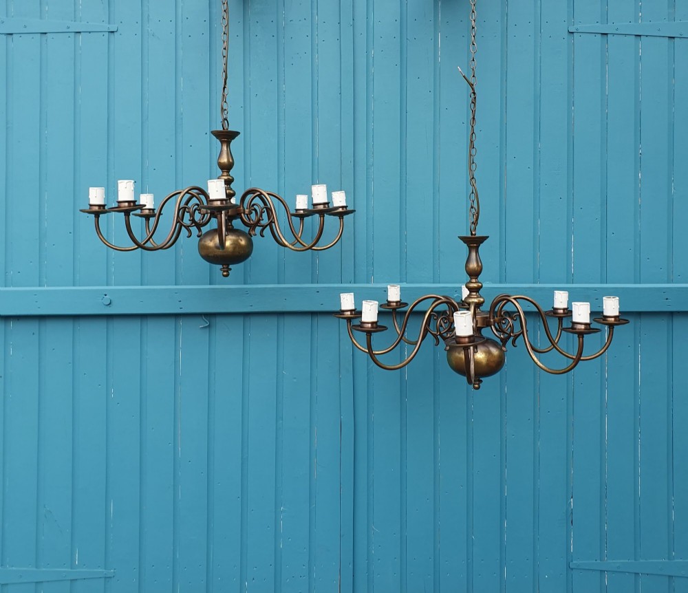 A pair of antique Dutch Flemish brass chandeliers featuring multi-arm S-scroll branches and central baluster stems with hanging chains.