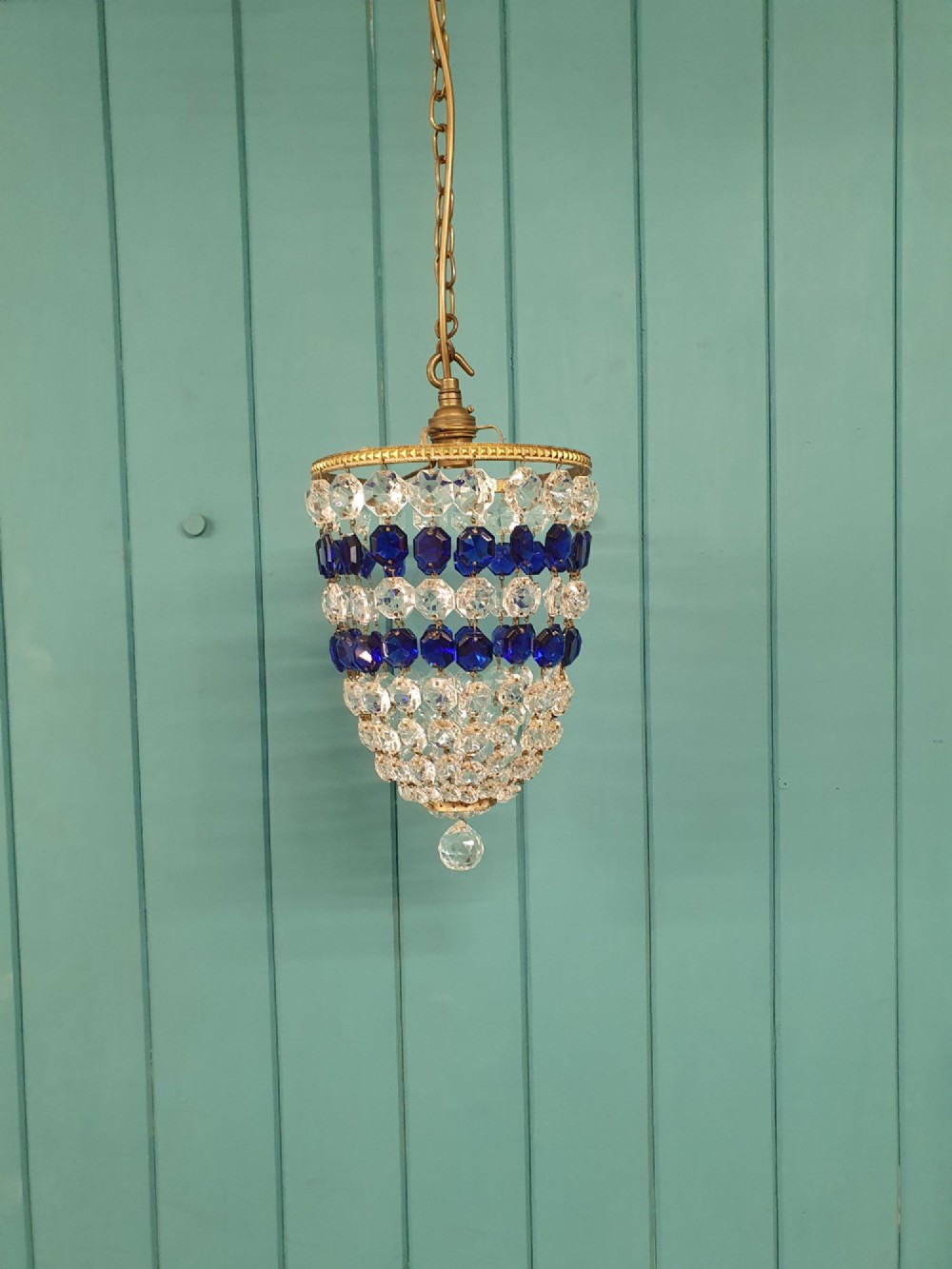 A small antique crystal bag chandelier featuring alternating concentric bands of clear and cobalt blue faceted glass beads suspended from a decorative brass rim and hanging chain.