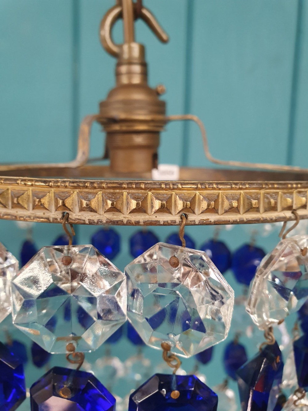 A small antique crystal bag chandelier featuring alternating concentric bands of clear and cobalt blue faceted glass beads suspended from a decorative brass rim and hanging chain. View III