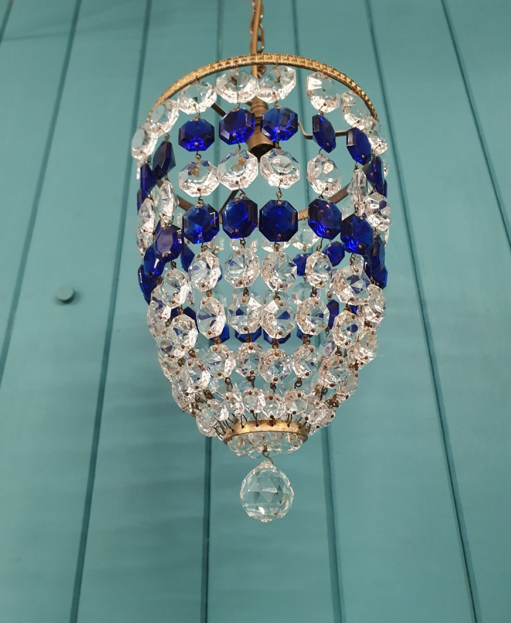 A small antique crystal bag chandelier featuring alternating concentric bands of clear and cobalt blue faceted glass beads suspended from a decorative brass rim and hanging chain. View IV