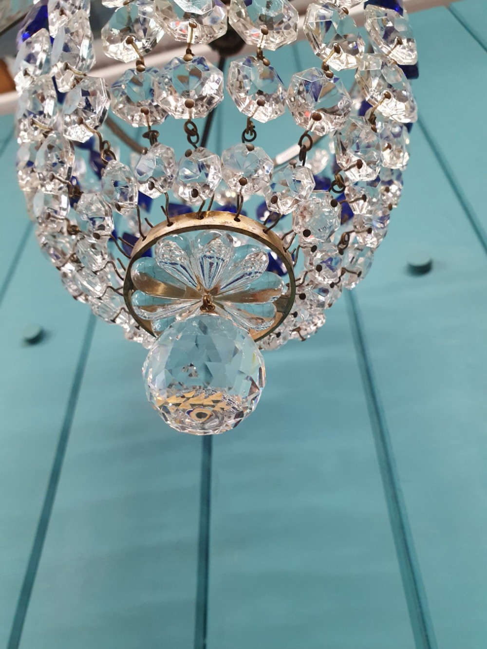 A small antique crystal bag chandelier featuring alternating concentric bands of clear and cobalt blue faceted glass beads suspended from a decorative brass rim and hanging chain. View V