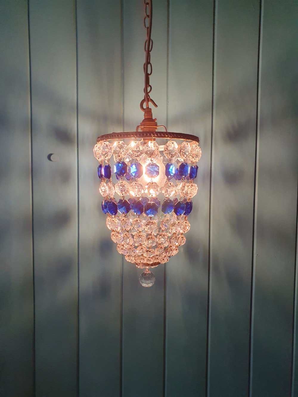 A small antique crystal bag chandelier featuring alternating concentric bands of clear and cobalt blue faceted glass beads suspended from a decorative brass rim and hanging chain. View VI