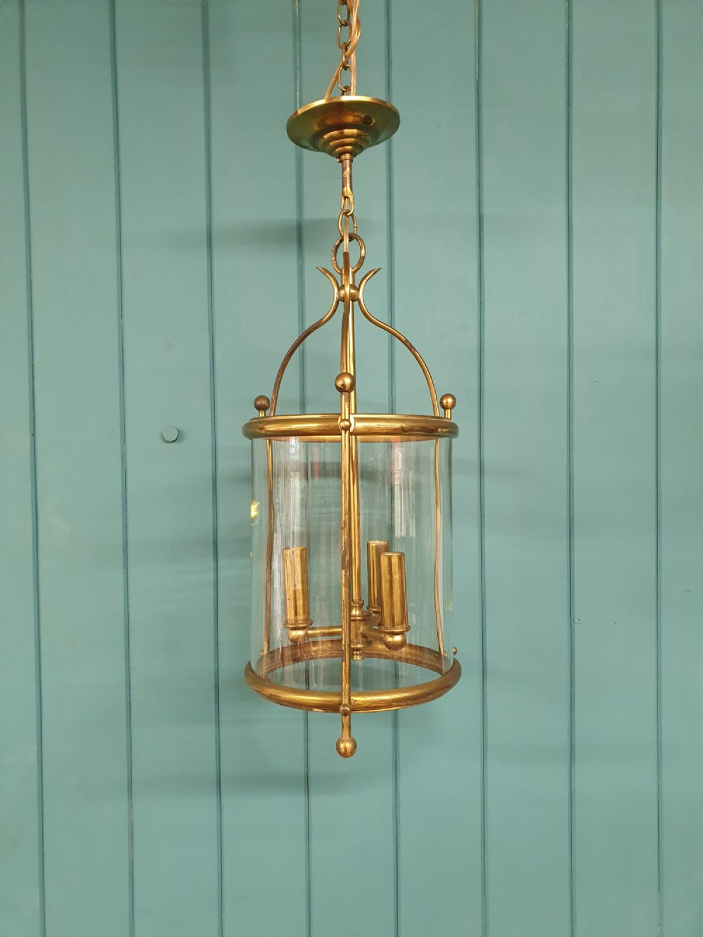 An early 20th-century brass hall lantern with a cylindrical glass shade, internal light fitting, arched crown top, and suspension chain.