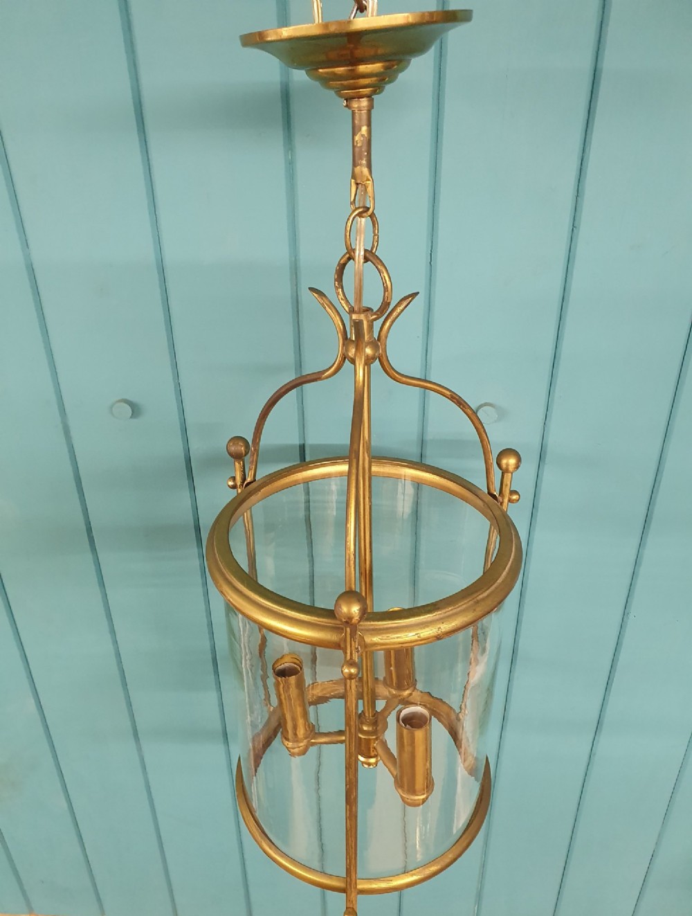 An early 20th-century brass hall lantern with a cylindrical glass shade, internal light fitting, arched crown top, and suspension chain. View II