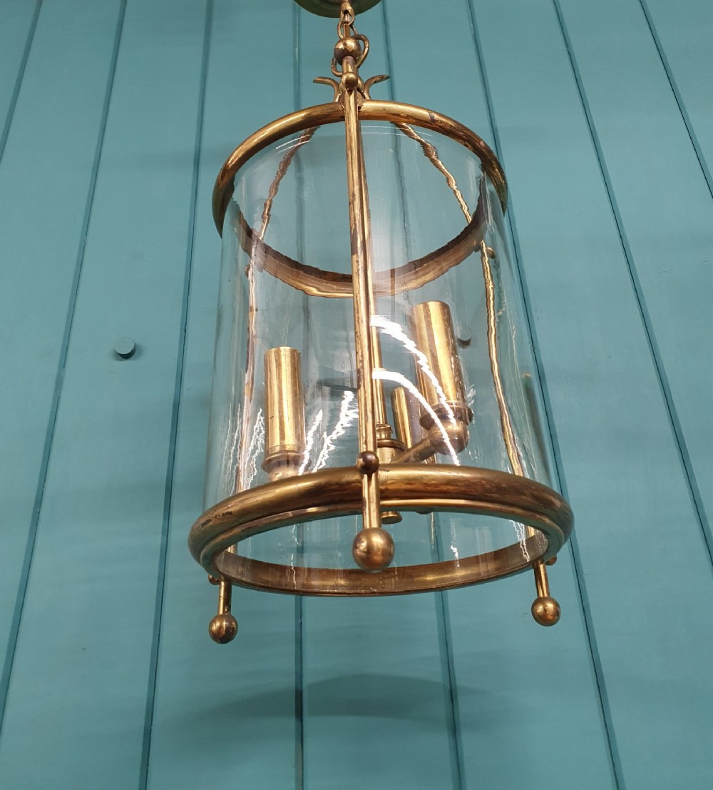 An early 20th-century brass hall lantern with a cylindrical glass shade, internal light fitting, arched crown top, and suspension chain. View III