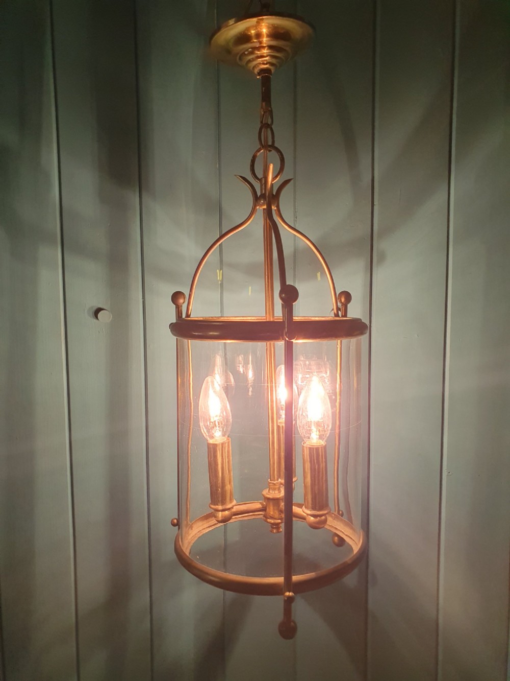 An early 20th-century brass hall lantern with a cylindrical glass shade, internal light fitting, arched crown top, and suspension chain. View VI