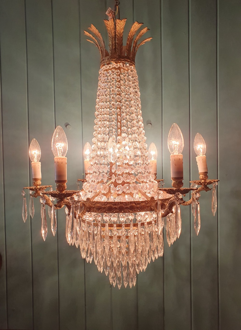 A six-arm brass tent chandelier decorated with crystal beads, drop pendants, and a leaf corona at the top. View V