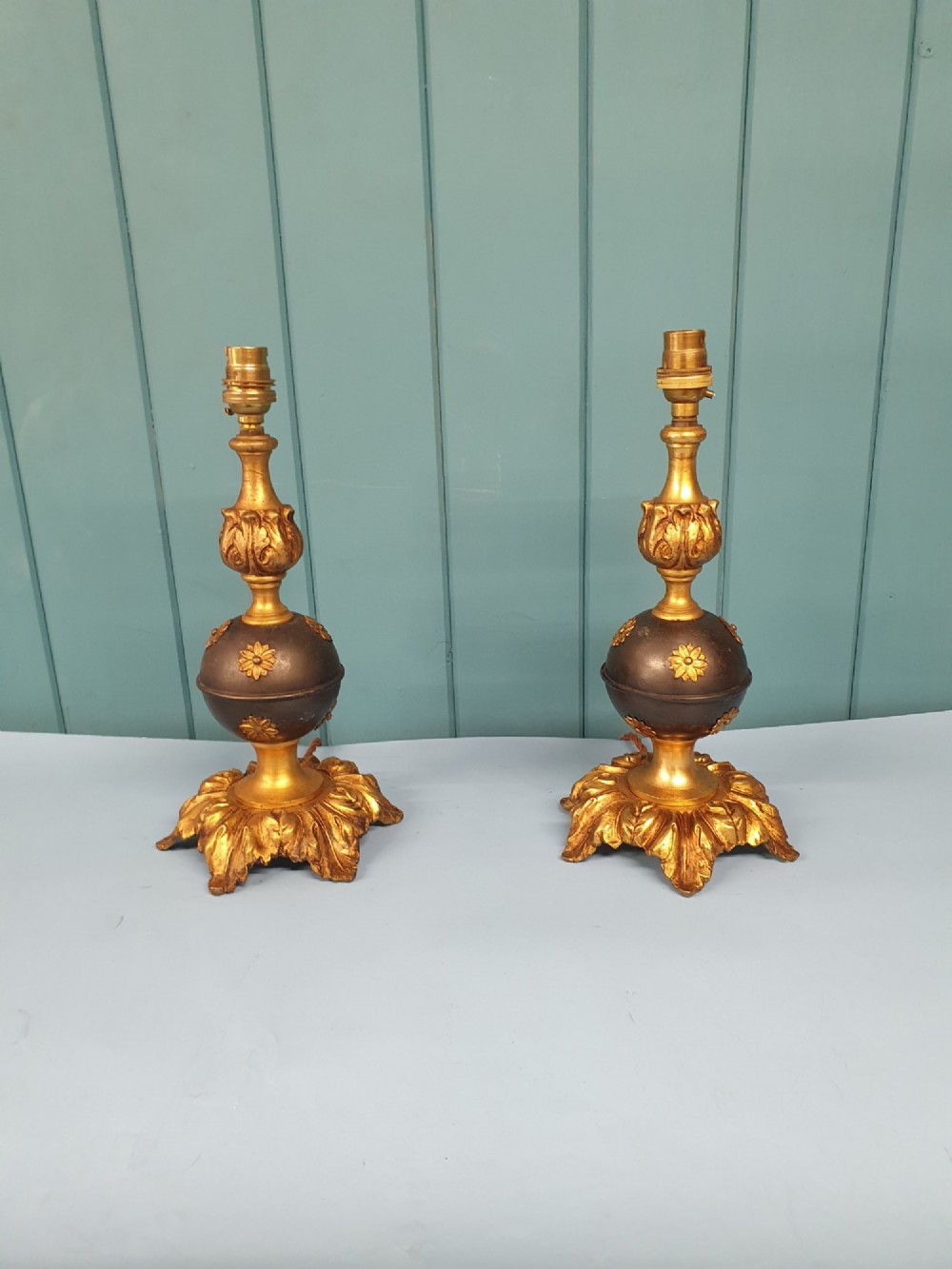 A pair of early 20th-century gilt brass table lamps featuring flared acanthus leaf bases, dark spherical central sections with gold floral mounts, and turned upper columns.