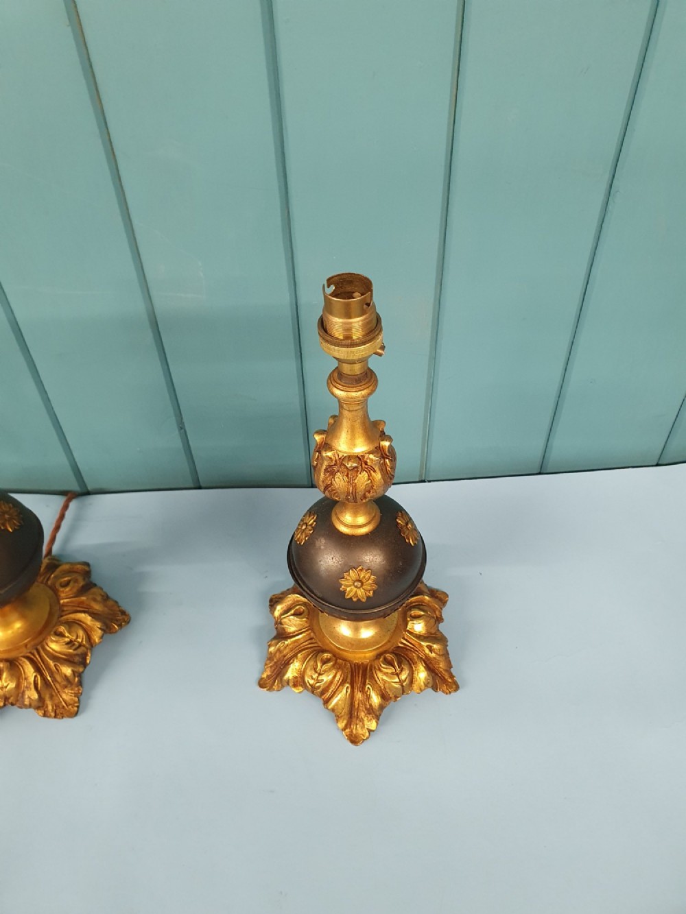A pair of early 20th-century gilt brass table lamps featuring flared acanthus leaf bases, dark spherical central sections with gold floral mounts, and turned upper columns. View II