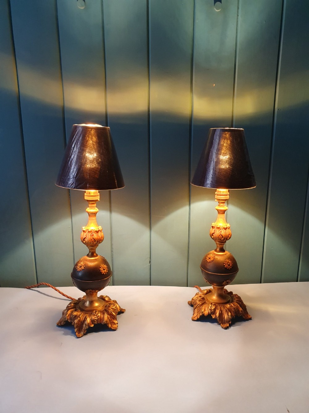 A pair of early 20th-century gilt brass table lamps featuring flared acanthus leaf bases, dark spherical central sections with gold floral mounts, and turned upper columns. View VI