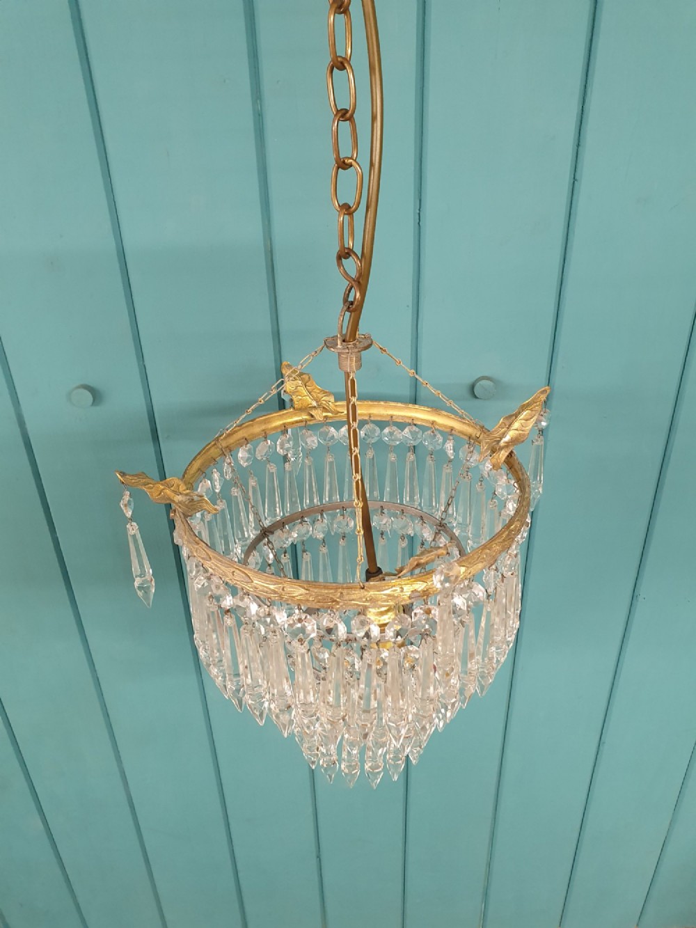 An antique three-tiered crystal chandelier featuring pointed prism spikes suspended from an ornate brass ring and central hanging chain. View II