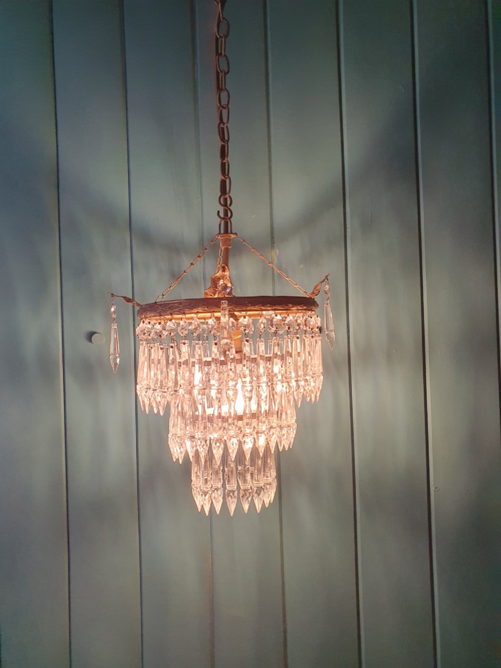 An antique three-tiered crystal chandelier featuring pointed prism spikes suspended from an ornate brass ring and central hanging chain. View V