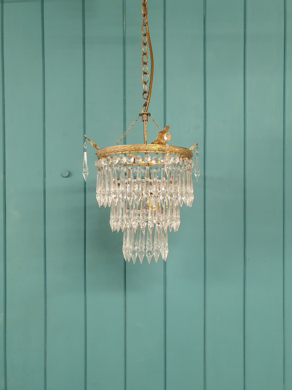 An antique three-tiered crystal chandelier featuring pointed prism spikes suspended from an ornate brass ring and central hanging chain.