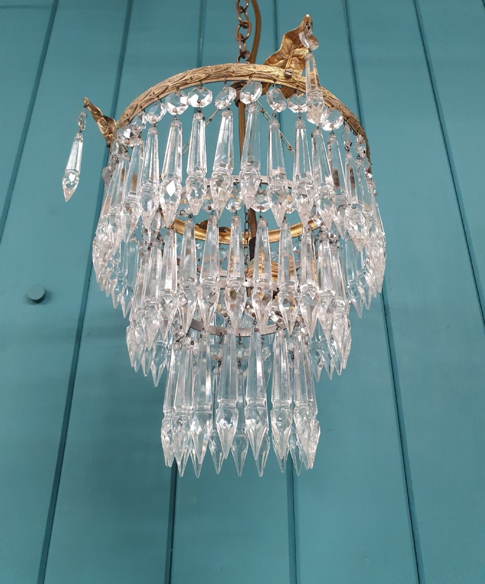An antique three-tiered crystal chandelier featuring pointed prism spikes suspended from an ornate brass ring and central hanging chain. View VI