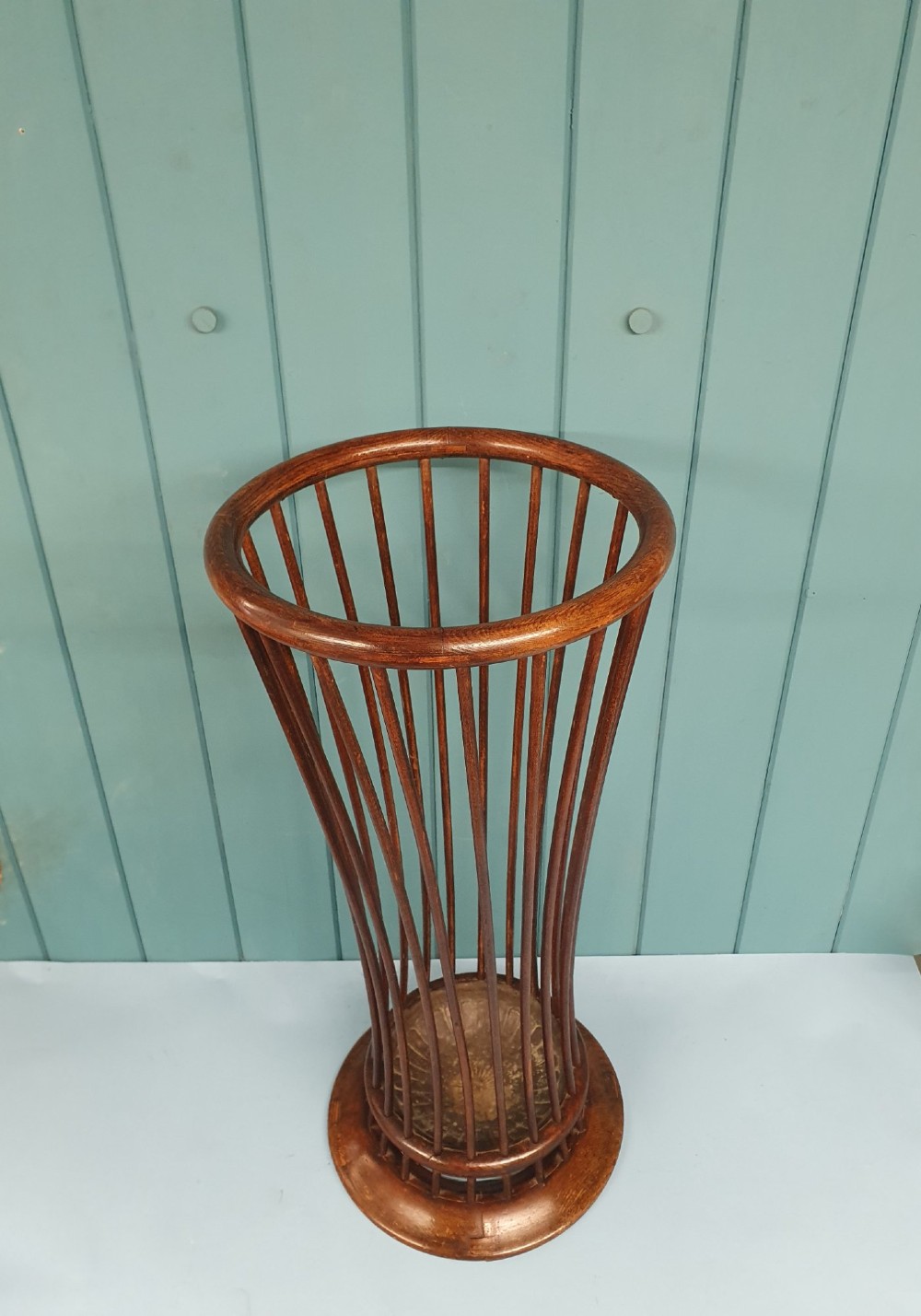 An early 20th-century oak stick stand featuring a flared, circular slatted framework tapering at the centre with an integrated metal drip tray at the circular base. View IV