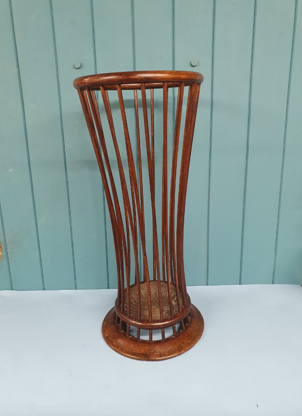 An early 20th-century oak stick stand featuring a flared, circular slatted framework tapering at the centre with an integrated metal drip tray at the circular base.