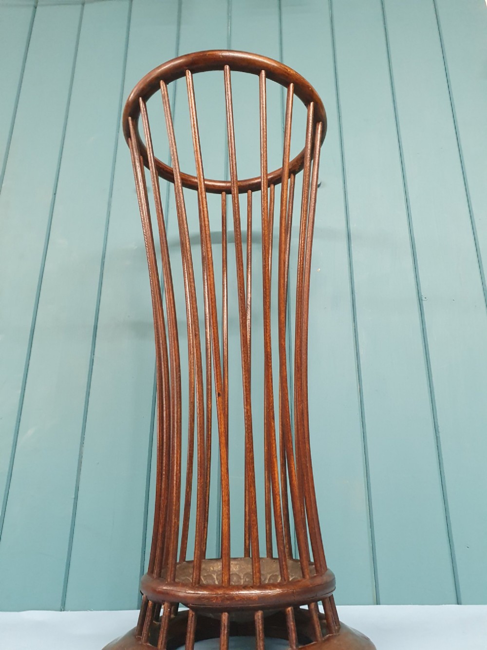 An early 20th-century oak stick stand featuring a flared, circular slatted framework tapering at the centre with an integrated metal drip tray at the circular base. View V