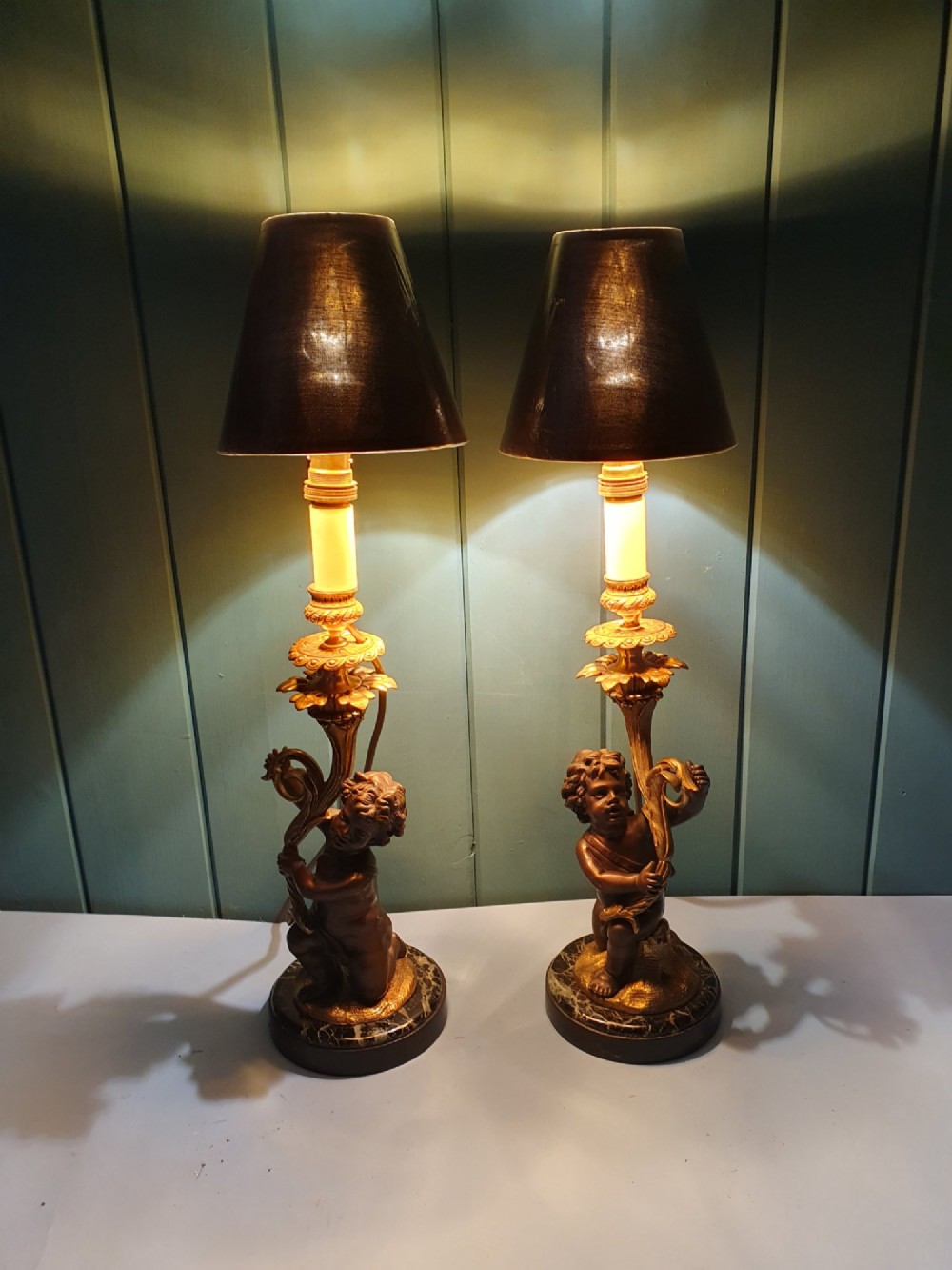 A pair of 1920s French-style dark bronze cherub table lamps with gilt foliate stems set on round black marble bases. View VIII