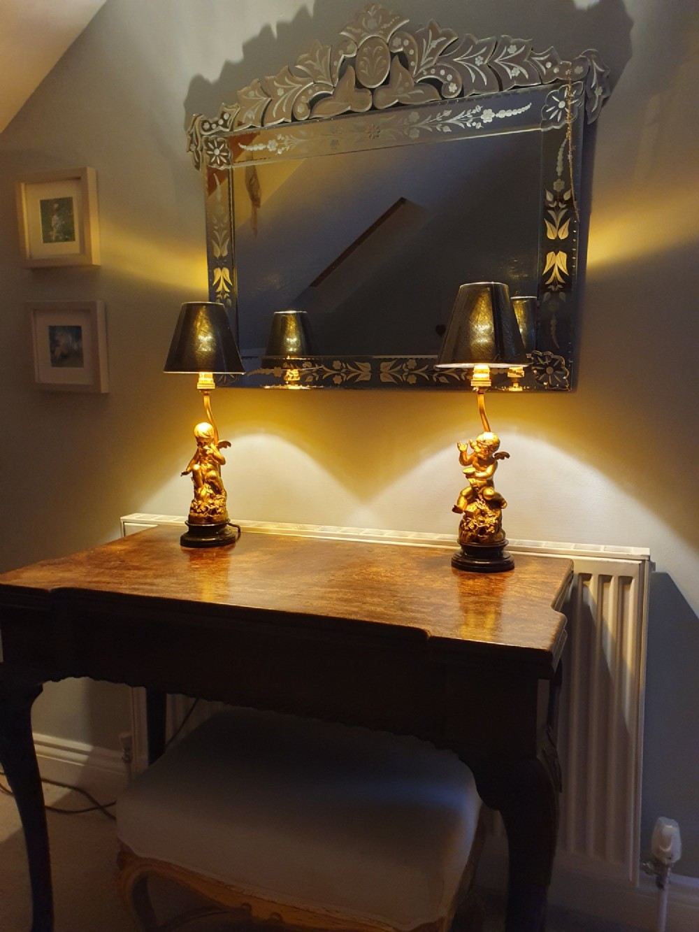 A pair of antique gilt brass table lamps featuring detailed sculpted cherub figures seated on circular dark marble bases. View V