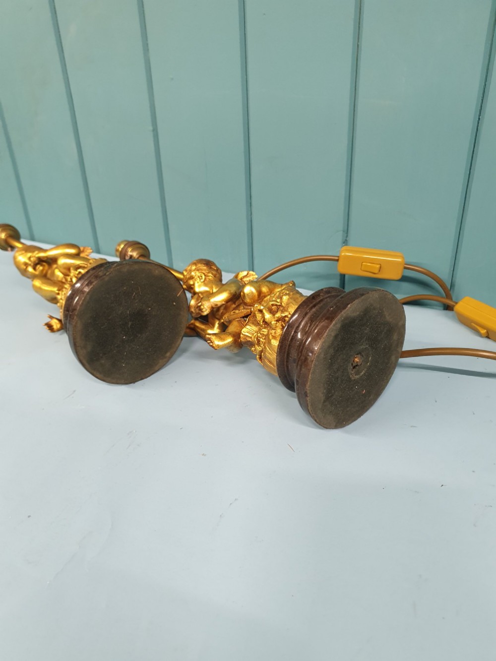 A pair of antique gilt brass table lamps featuring detailed sculpted cherub figures seated on circular dark marble bases. View VII