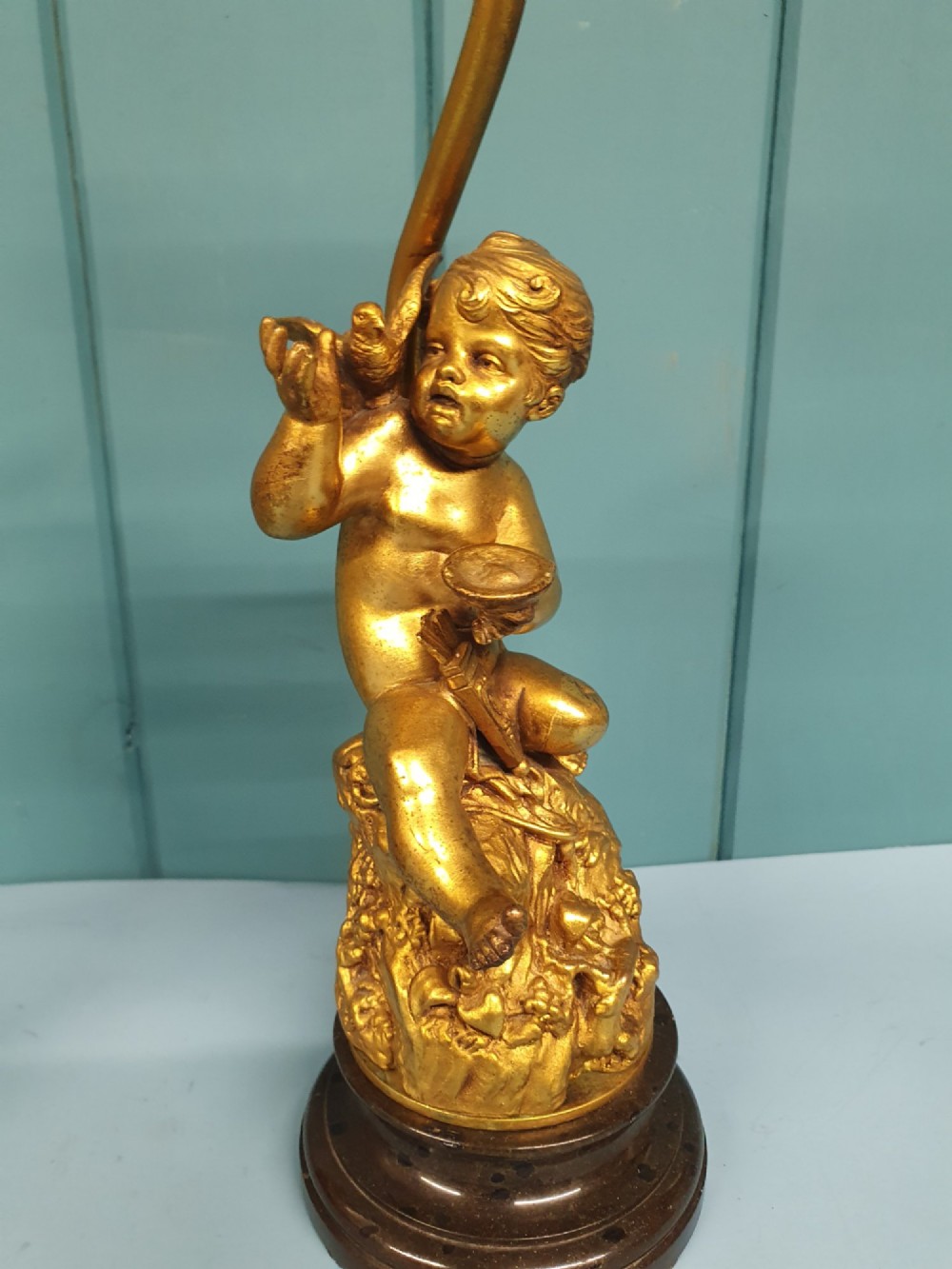 A pair of antique gilt brass table lamps featuring detailed sculpted cherub figures seated on circular dark marble bases. View IX