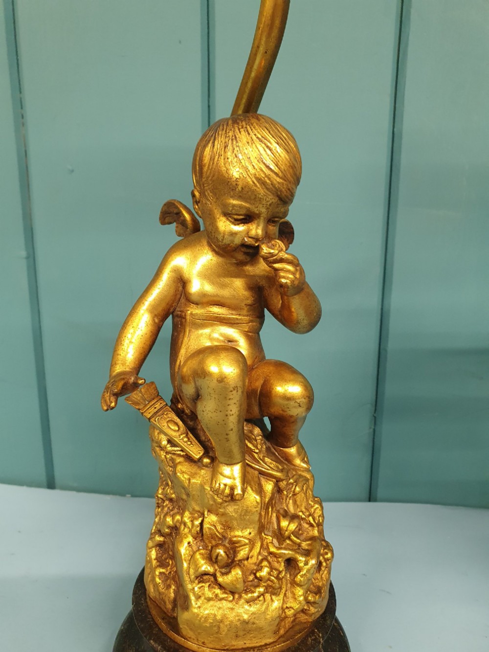 A pair of antique gilt brass table lamps featuring detailed sculpted cherub figures seated on circular dark marble bases. View X