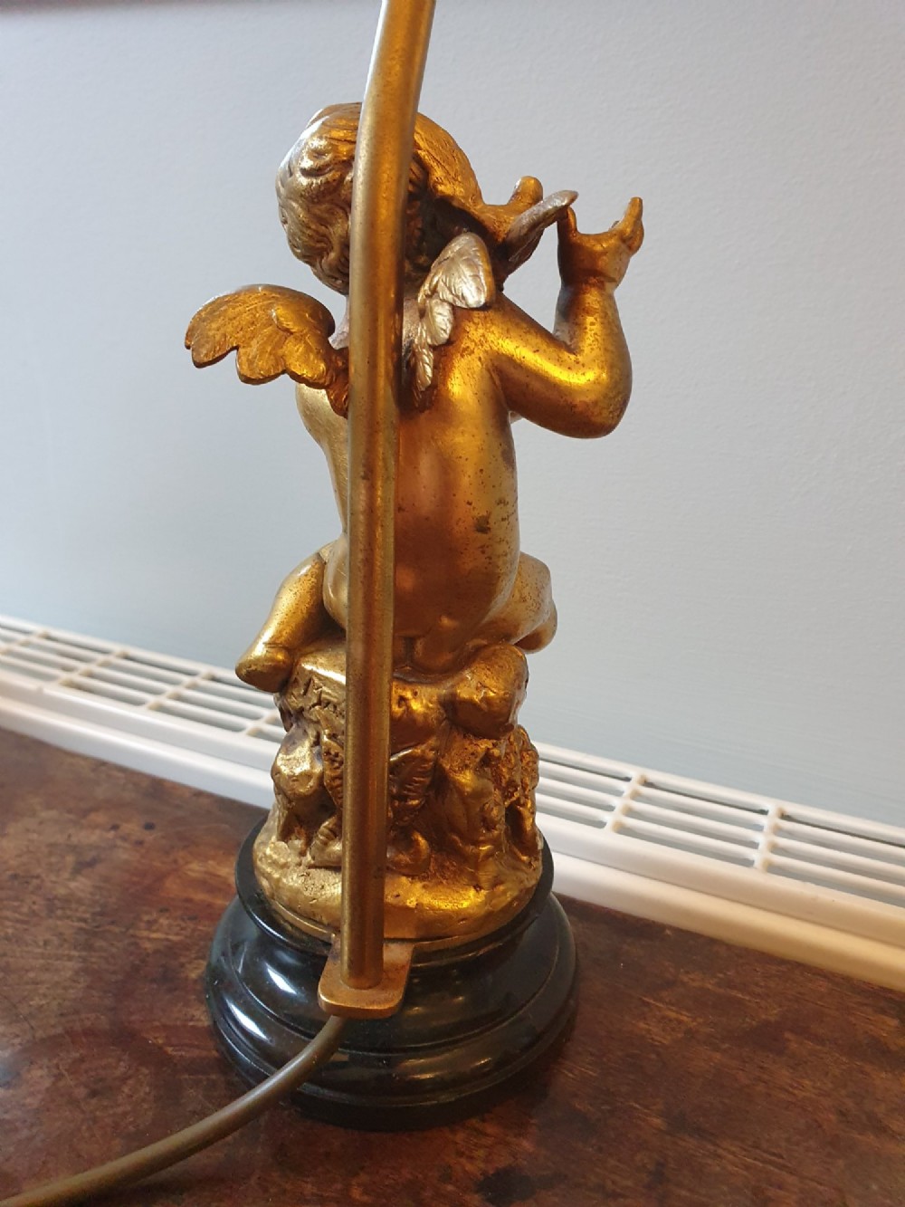A pair of antique gilt brass table lamps featuring detailed sculpted cherub figures seated on circular dark marble bases. View XII