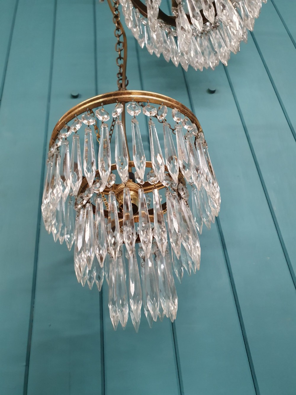 A set of three tiered brass pendant chandeliers featuring suspended clear crystal spike droplets. View II
