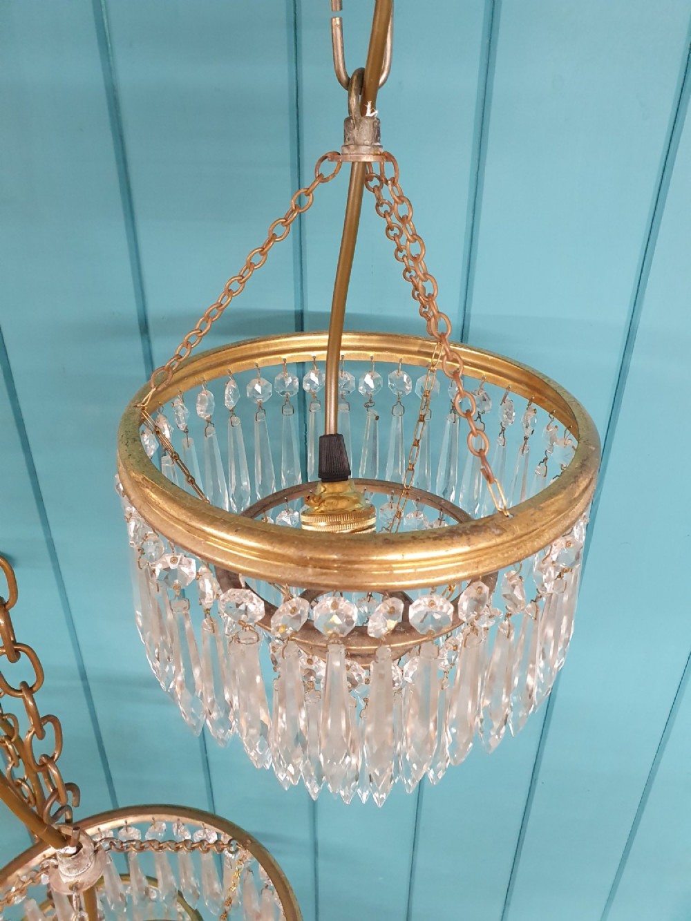 A set of three tiered brass pendant chandeliers featuring suspended clear crystal spike droplets. View III