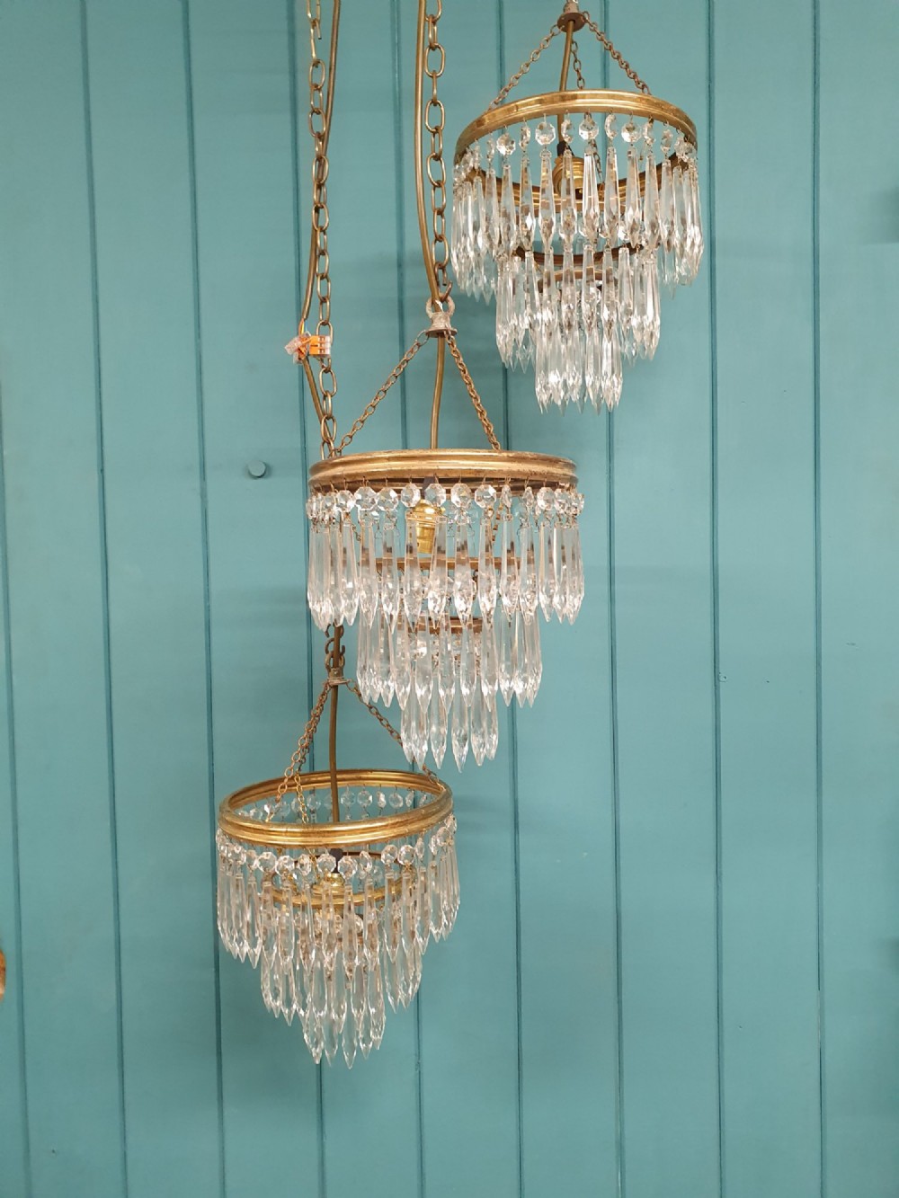 A set of three tiered brass pendant chandeliers featuring suspended clear crystal spike droplets.
