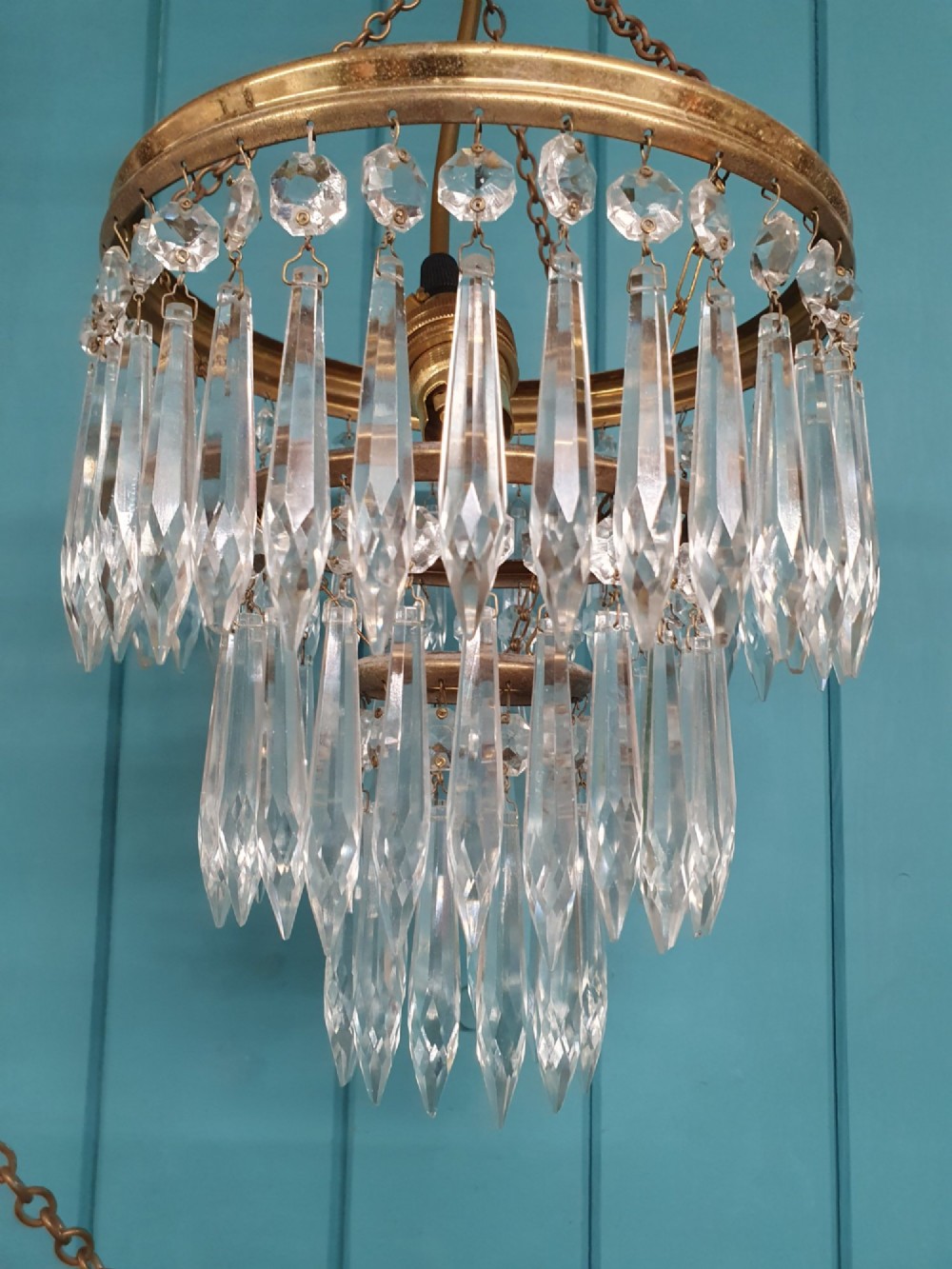A set of three tiered brass pendant chandeliers featuring suspended clear crystal spike droplets. View V