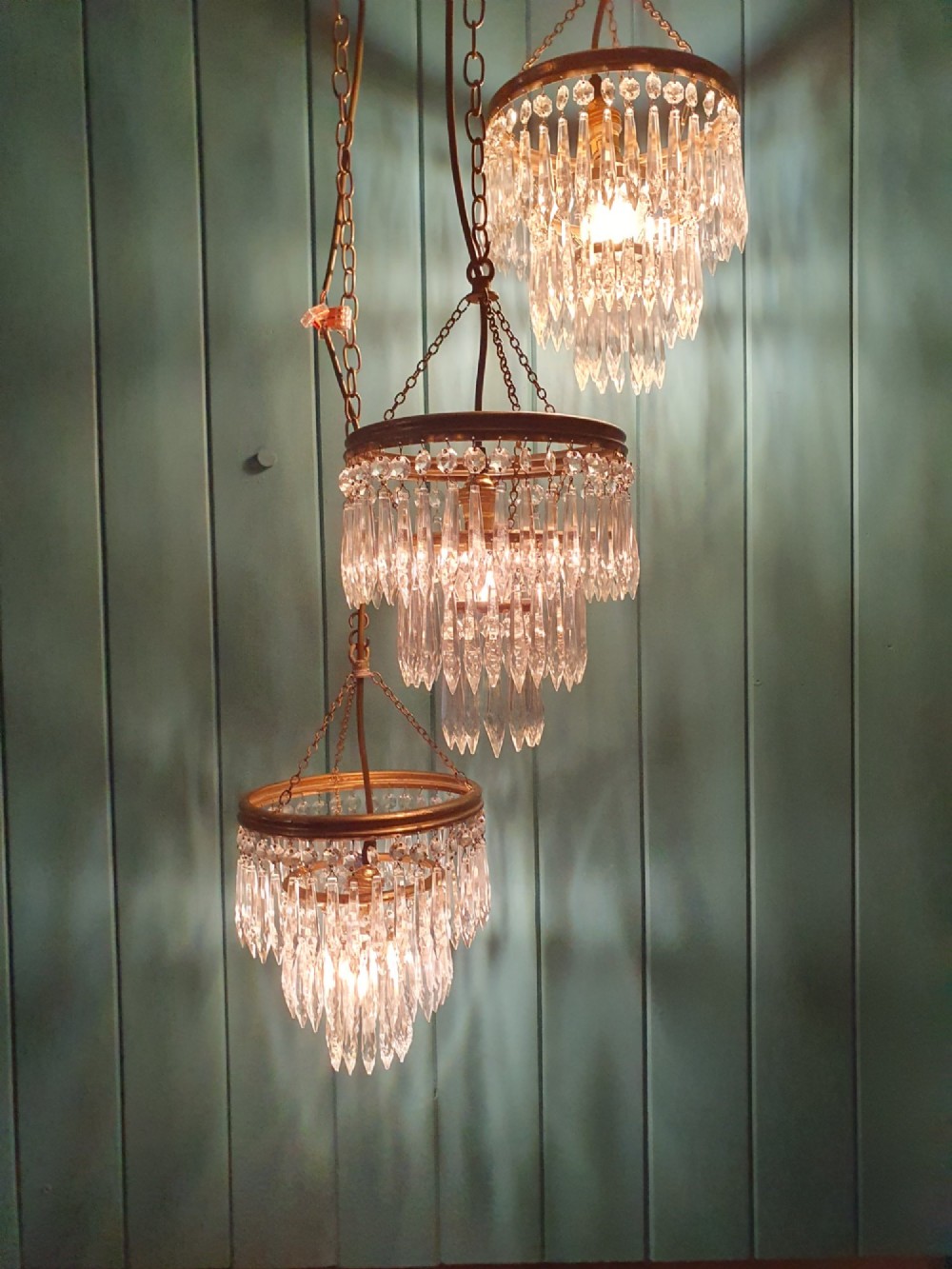 A set of three tiered brass pendant chandeliers featuring suspended clear crystal spike droplets. View VI