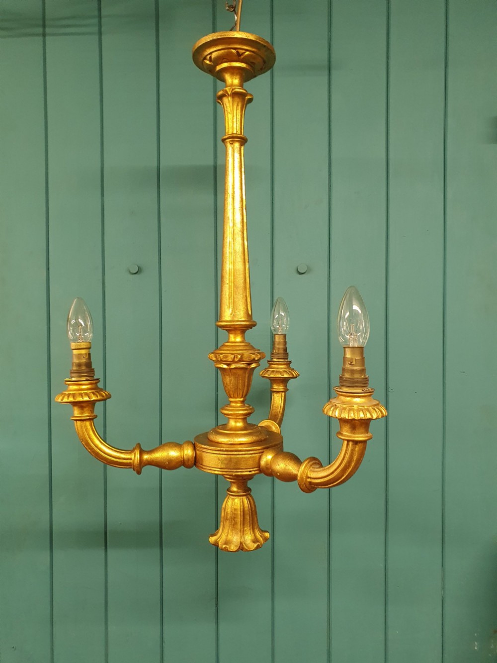 Circa 1900 carved giltwood three-arm chandelier featuring a central turned column, scrolled branches, fluted bottom drop, and three purple fabric lampshades.