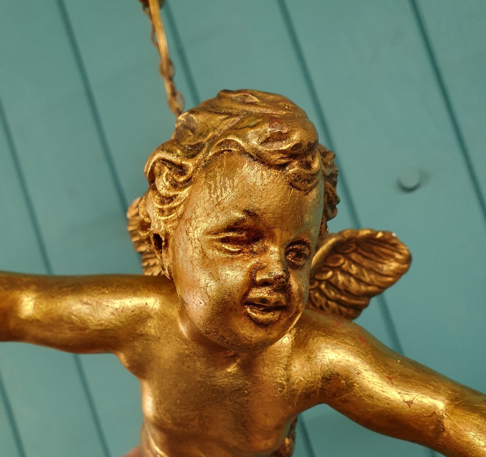 An antique gilt spelter flying winged cherub suspended from a chain, holding two light sockets decorated with cut glass crystal drops. View III