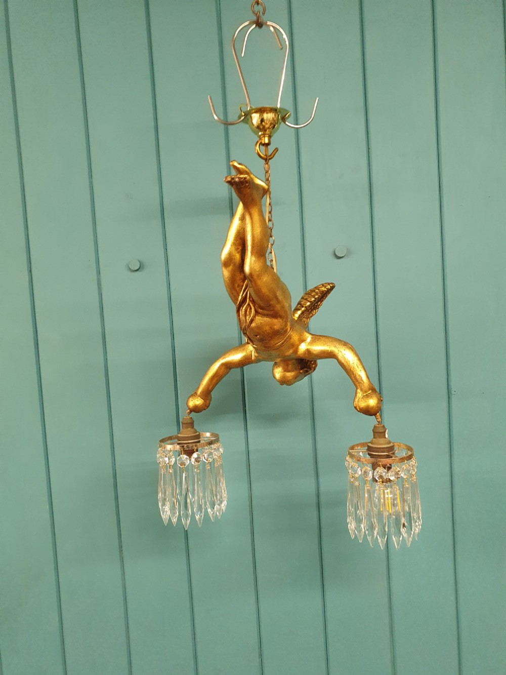 An antique gilt spelter flying winged cherub suspended from a chain, holding two light sockets decorated with cut glass crystal drops. View IV