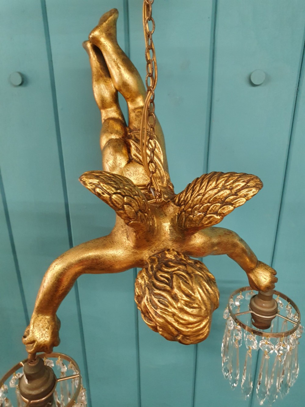 An antique gilt spelter flying winged cherub suspended from a chain, holding two light sockets decorated with cut glass crystal drops. View VI