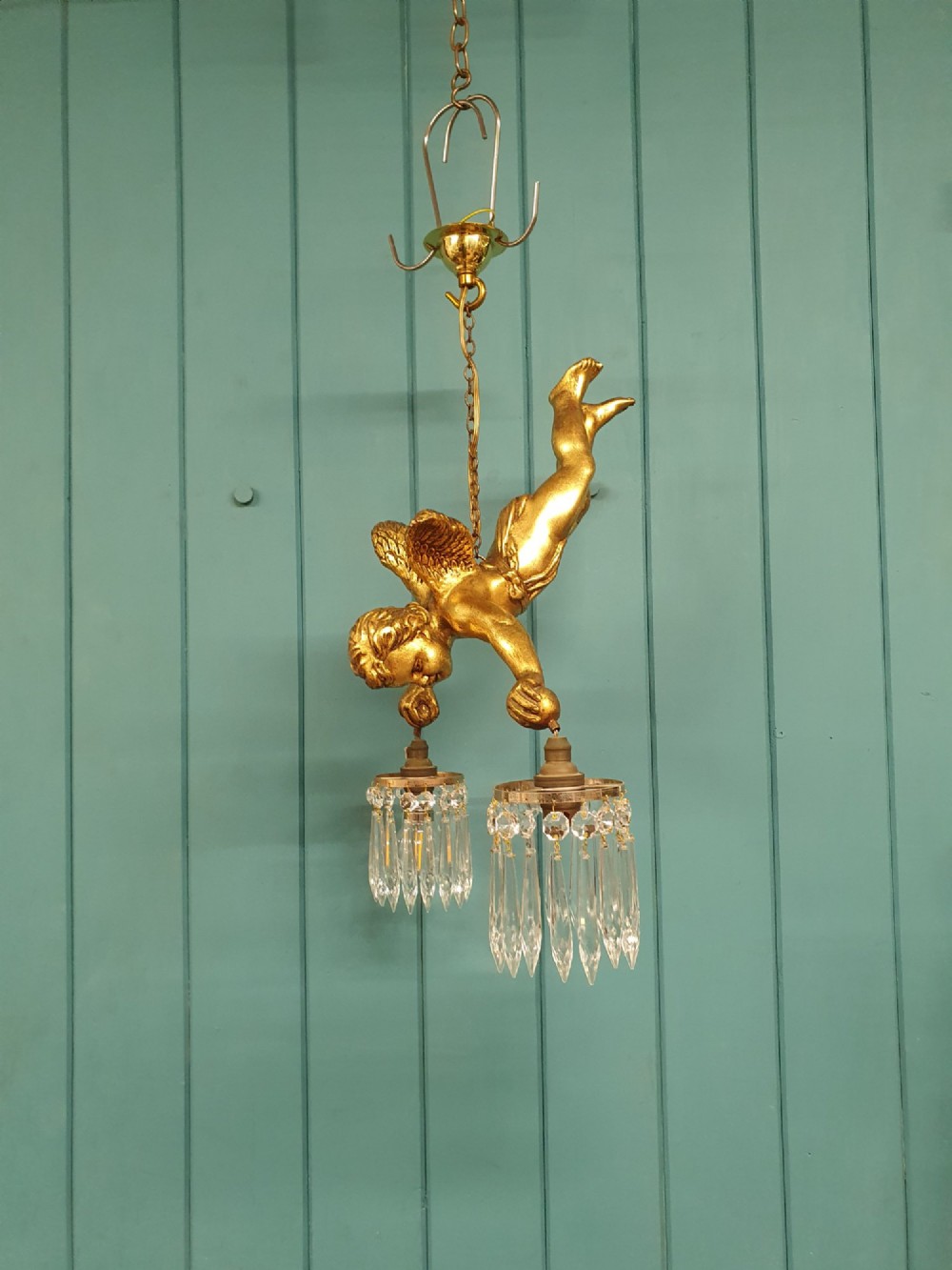 An antique gilt spelter flying winged cherub suspended from a chain, holding two light sockets decorated with cut glass crystal drops. View VII