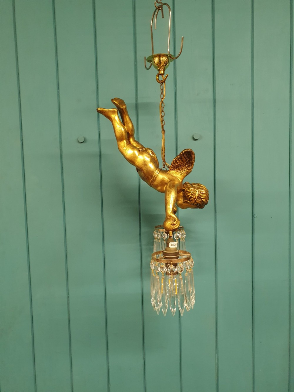 An antique gilt spelter flying winged cherub suspended from a chain, holding two light sockets decorated with cut glass crystal drops. View VIII