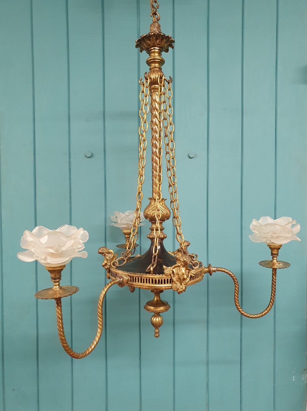 A French ebonised and brass three-arm chandelier featuring twisted metal arms, supporting chain suspension, and frosted glass shades shaped like open flowers. View V